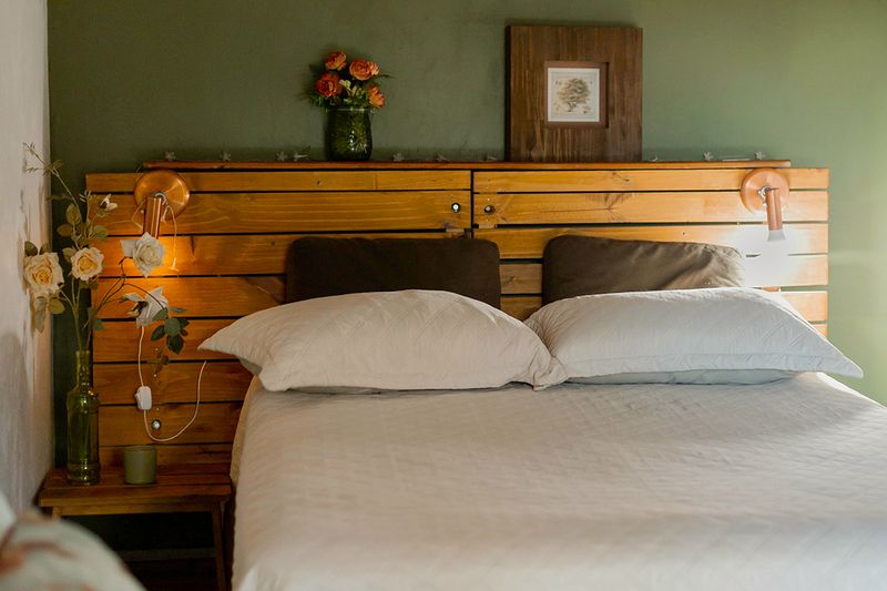 A sage green bedroom in a matte paint finish. There is a double bed with a wooden headboard and flowers on a nightstand.