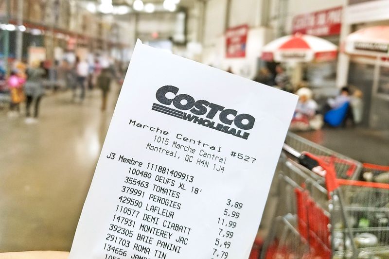 A Costco receipt in focus in front of a cart inside the warehouse store.