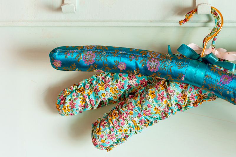 Three padded clothes hangers, all with floral patterns, on a single wall hook.