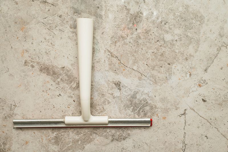 A squeegee with a white plastic handle on a flat marble surface, photographed from above.