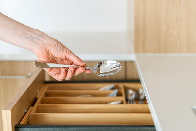 Anonymous person lifting a spoon out of a silverware drawer with a bamboo divider.