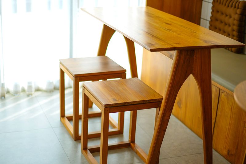 A small wooden table with long geometric legs and two matching wood stools.