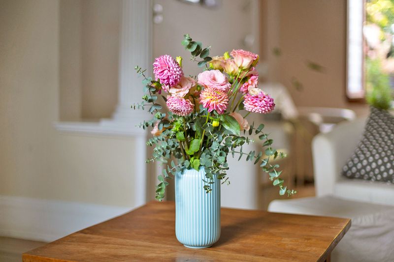 A bouquet of pink and green flowers in a blue fluted ceramic vase on a wooden tabletop.