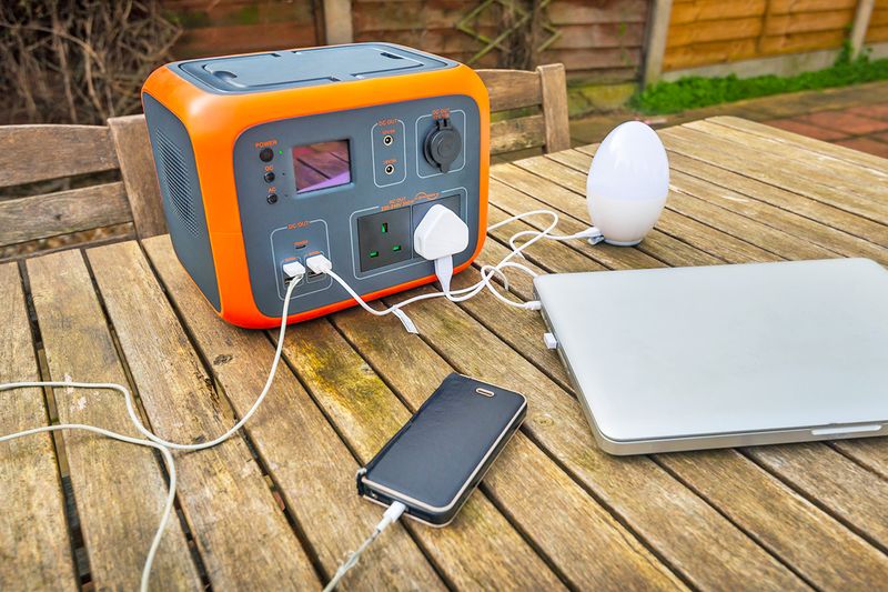 An unbranded portable power station with a phone, laptop, and lightbulb plugged into it for charging.
