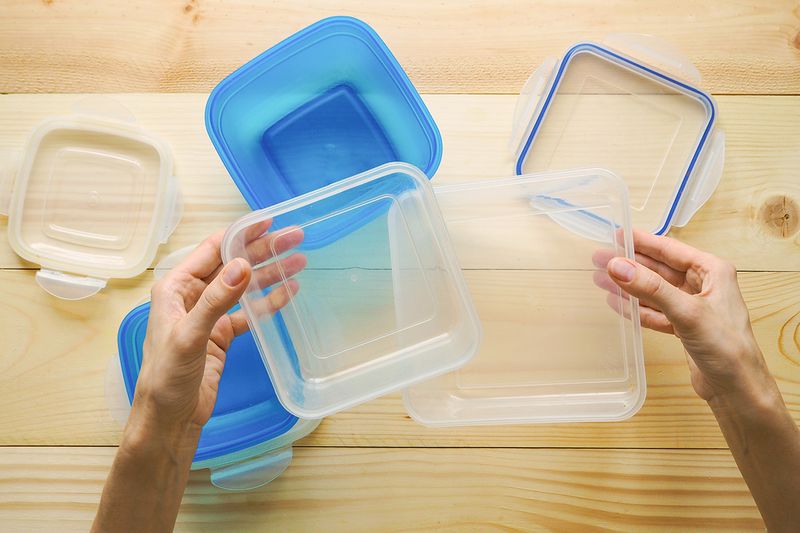 Anonymous person sorting plastic food containers and their lids on a wooden countertop. The hands and containers are shot from above.