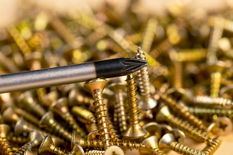 Close-up of a magnetized tip of a screwdriver picking up a gold screw in a large pile of them.