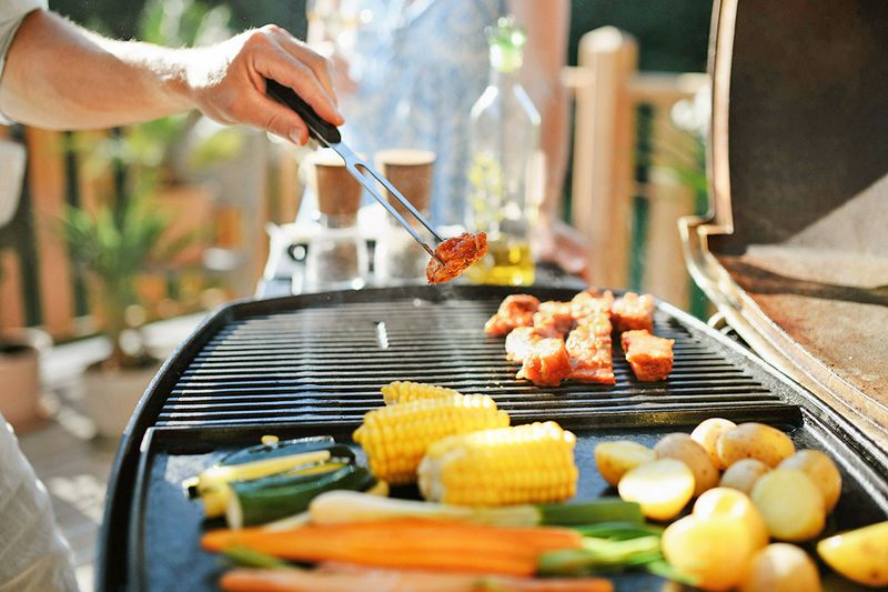 Anonymous person grilling meat on the grill grates and vegetables on a cast-iron griddle.
