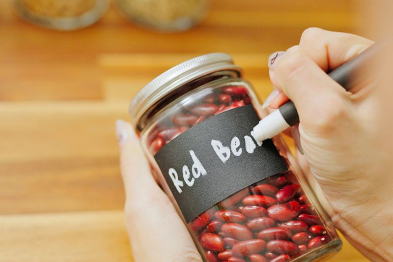 Anonymous person labeling a glass jar of dried red beans with a white chalk marker.