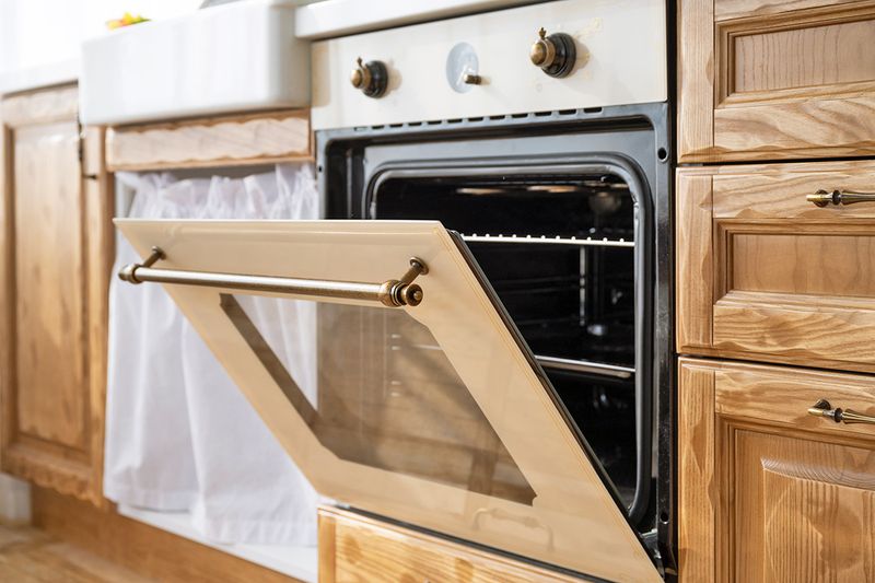 An ajar oven door in a kitchen with wood cabinetry and a sink skirt.