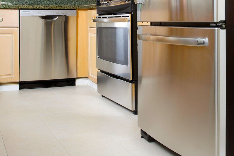 A lower view of a kitchen, showing the gaps under the stainless steel fridge, oven, and dishwasher.