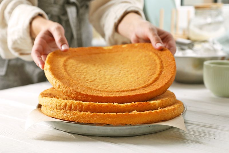 Anonymous person putting a third layer of unfrosted cake on top of two others.