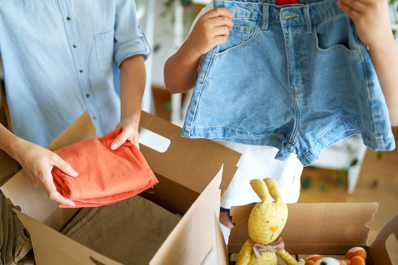 Two anonymous people folding clothes into cardboard boxes.