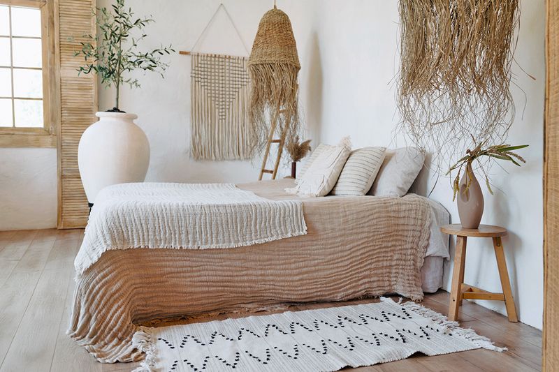 A boho-style bedroom with gauzy bedding, seagrass light fixtures, and a white and black geometric runner beside the bed.