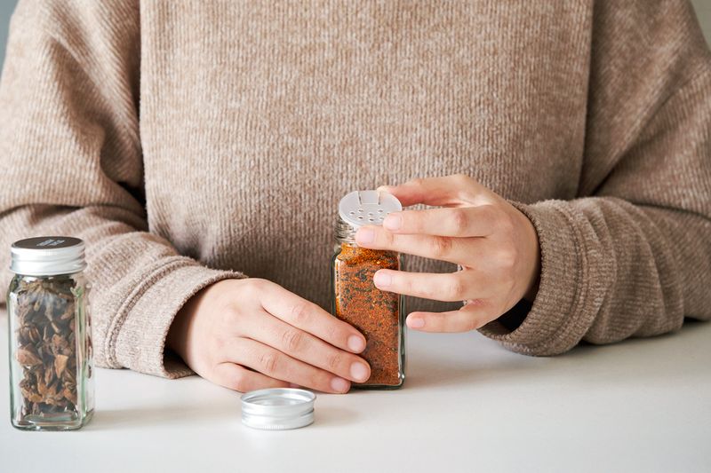 Anonymous person reattaching the shaker lid on a glass spice jar that appears to be filled with an original spice blend.
