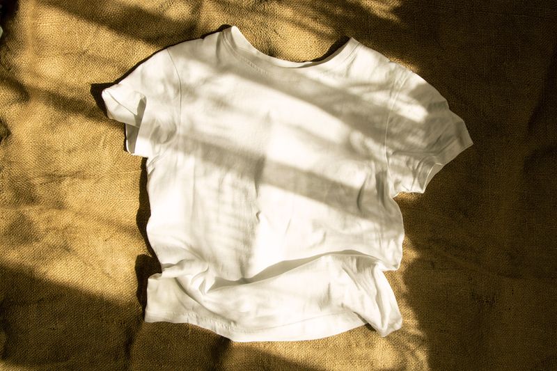 A white T-shirt against a burlap background with sunlight streaked across it.