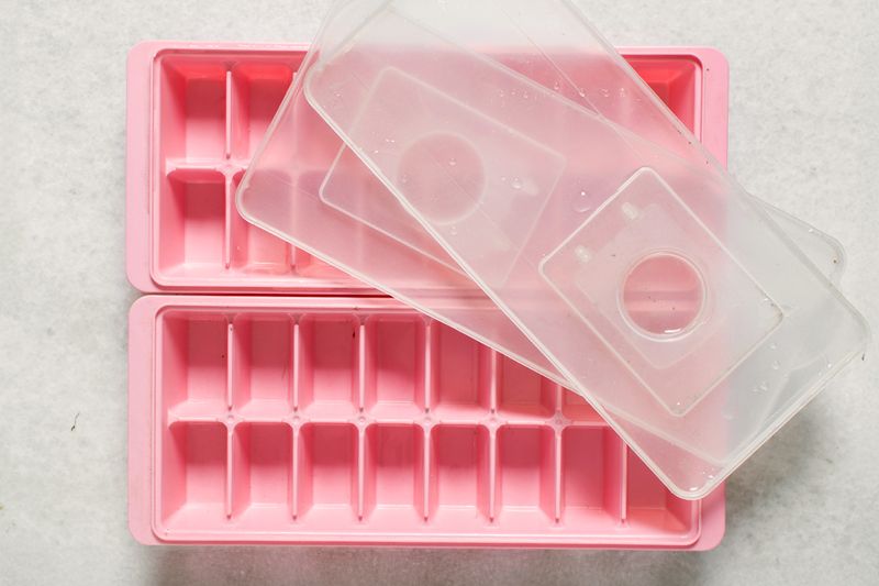 Two pink ice cube trays with clear lids photographed from above against a white background.