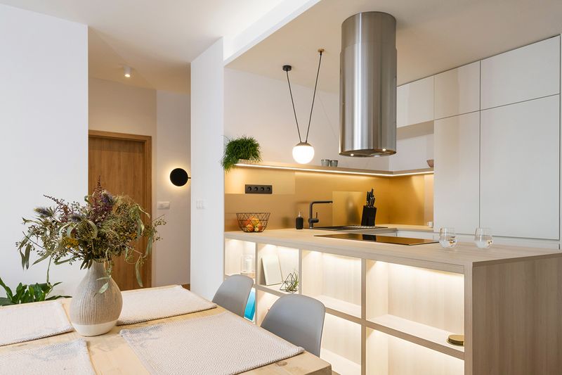 A modern-looking kitchen in a condo with a pendant light over the countertop, under-cabinet lighting, and a sconce by the front door.