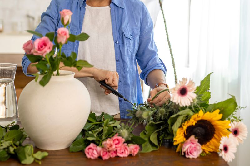 Anonymous person trimming individual flowers and arranging them in a large white ceramic vase.