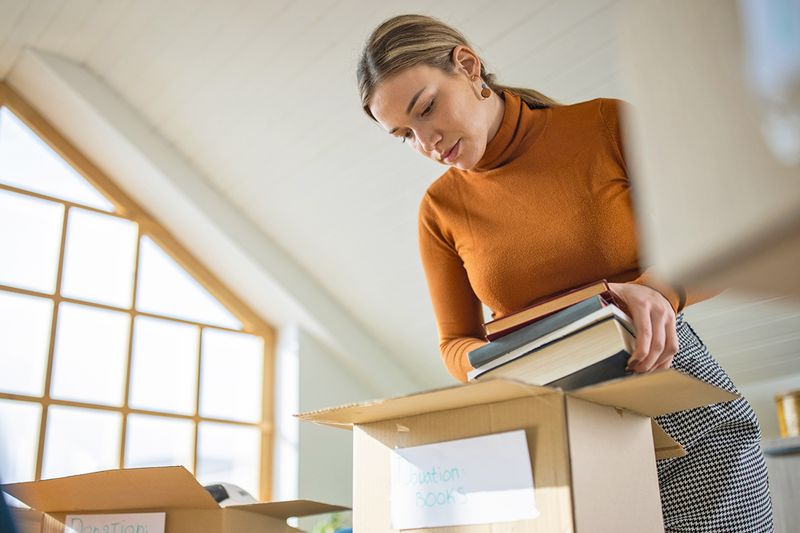 Young woman putting a stack of books into a box labeled "donation books."