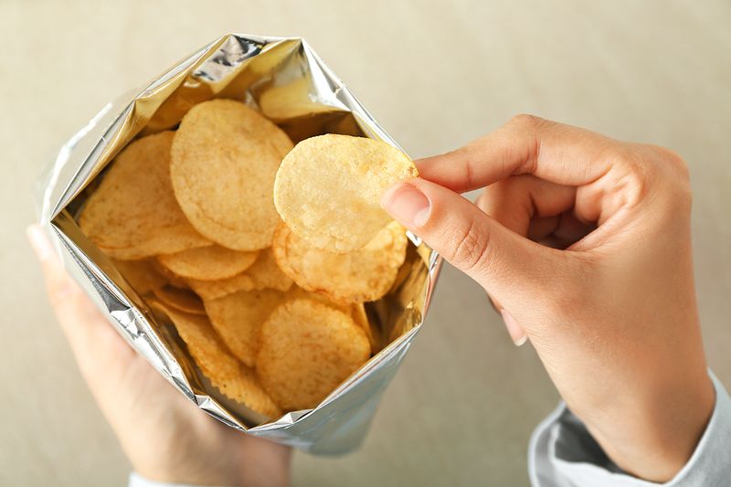 An anonymous person taking a potato chip out of an open bag that's shot from above.