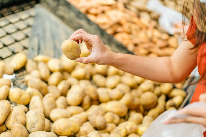 Woman picking out a gold potato from a large pile of them.