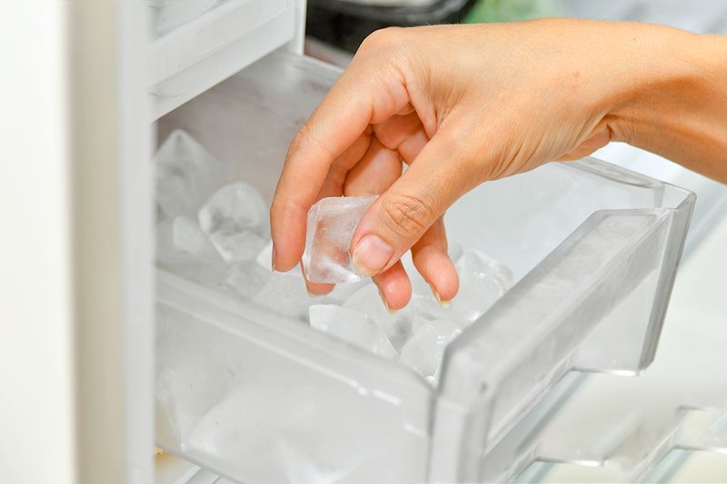 Person reaching into their freezer's ice storage bin to get a few cubes.