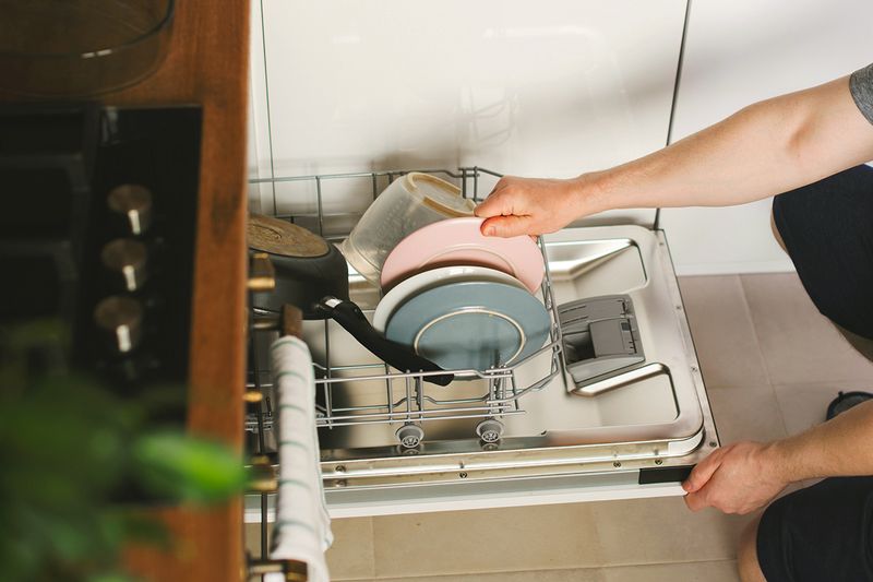 An anonymous person loading a dishwasher with plates, bowls, and a pan.