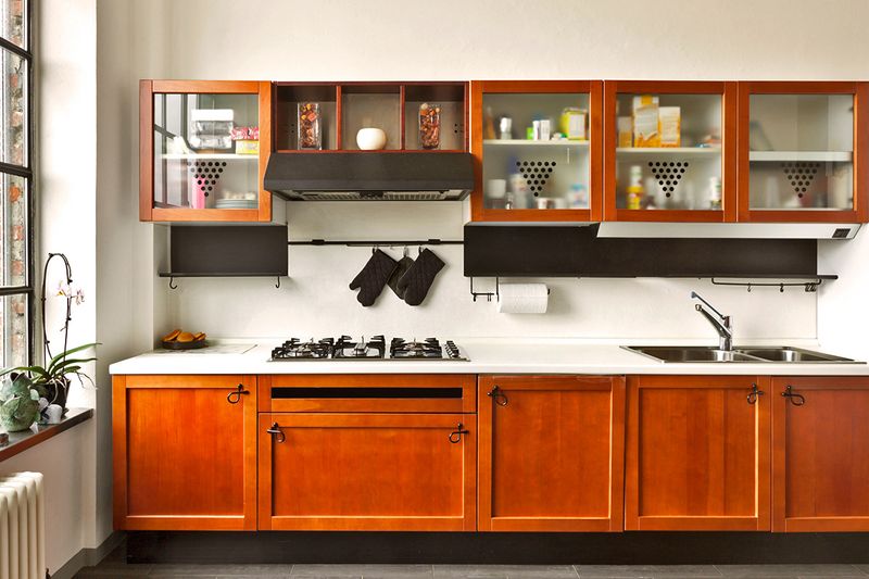 A kitchen in a loft with wood cabinets and a white countertop. The kitchen is linear and the upper cabinets do not go all the way to the ceiling.