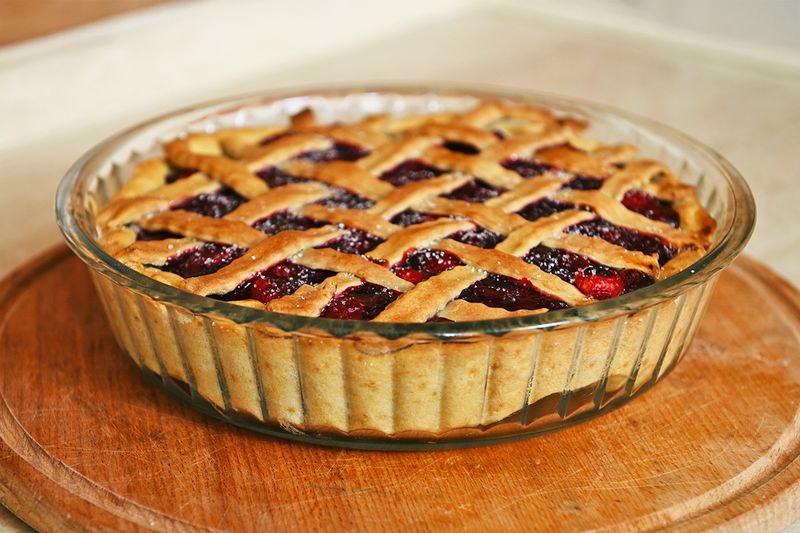 A cherry pie with a lattice crust in a glass baking dish on a wooden trivet.