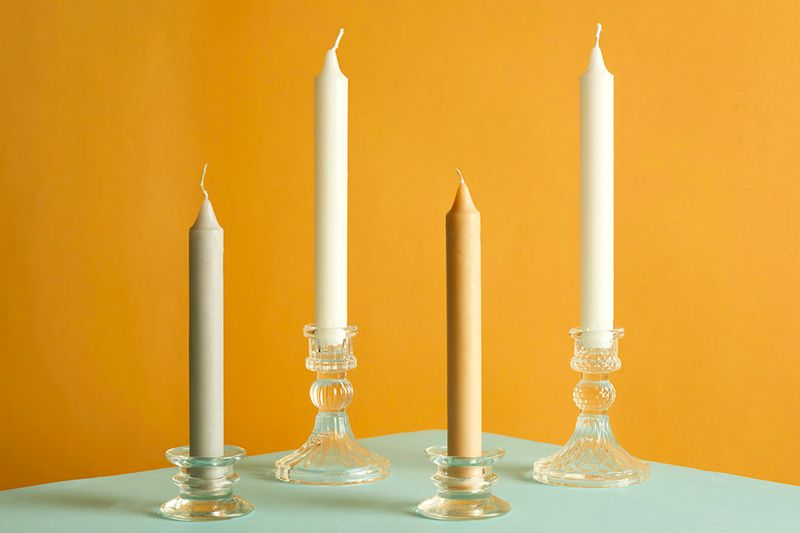 Four plain taper candles in glass holders against a dark yellow background.