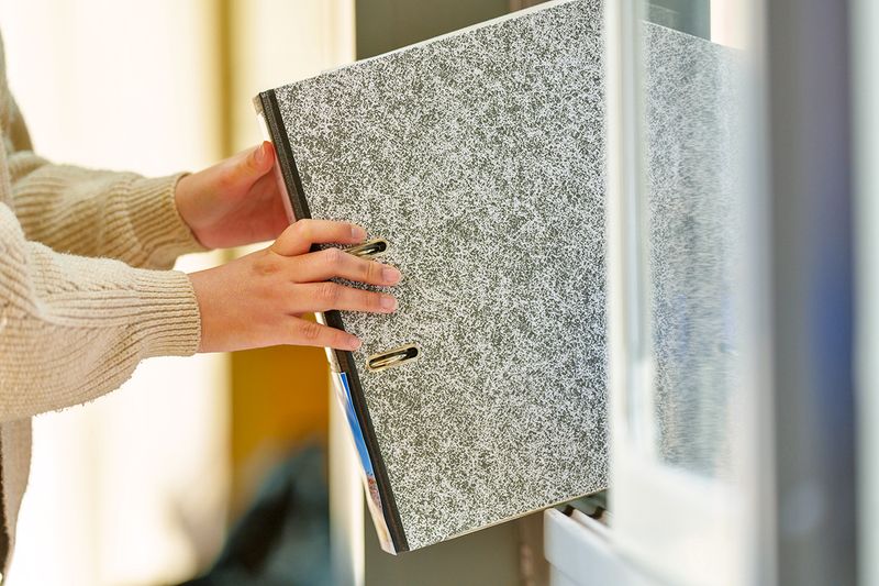 Anonymous person returning a gray, three-ring binder to a bookshelf.