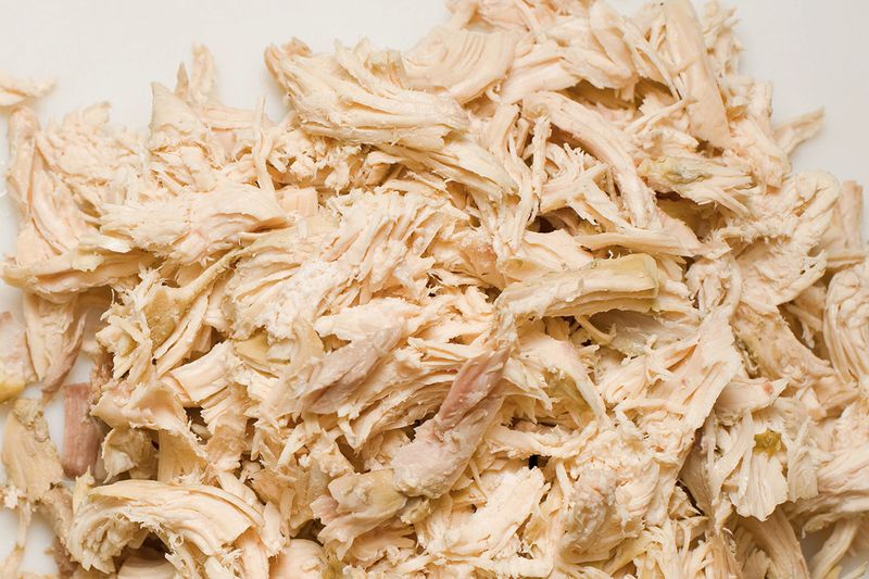 A close-up of finely shredded cooked chicken against a white background.