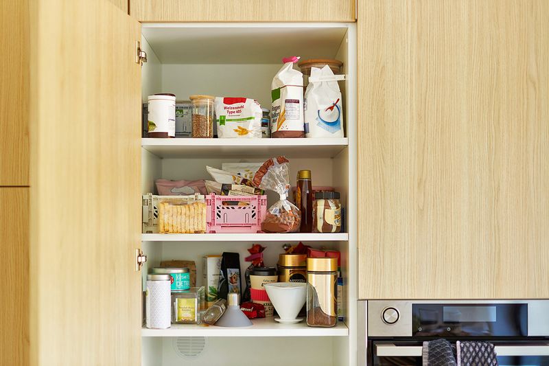 An open kitchen cabinet revealing three rows of well-organized pantry goods.