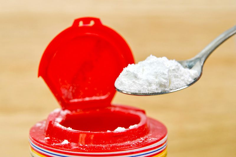 A suspended spoon of baking powder next to a red container.