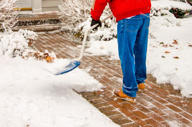 Anonymous person shoveling snow off a brick walkway.