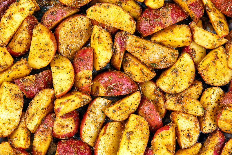 A close-up shot of well-seasoned, oven roasted potatoes cut into wedges.