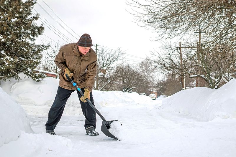 Middle-aged man shoveling snow from a driveway.