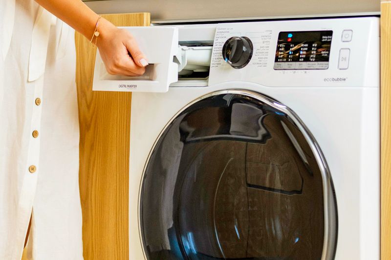 Anonymous woman pulling out the detergent drawer in a front-load washing machine.