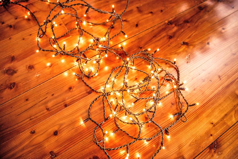 A tangled strand of lit Christmas lights on a wood floor.