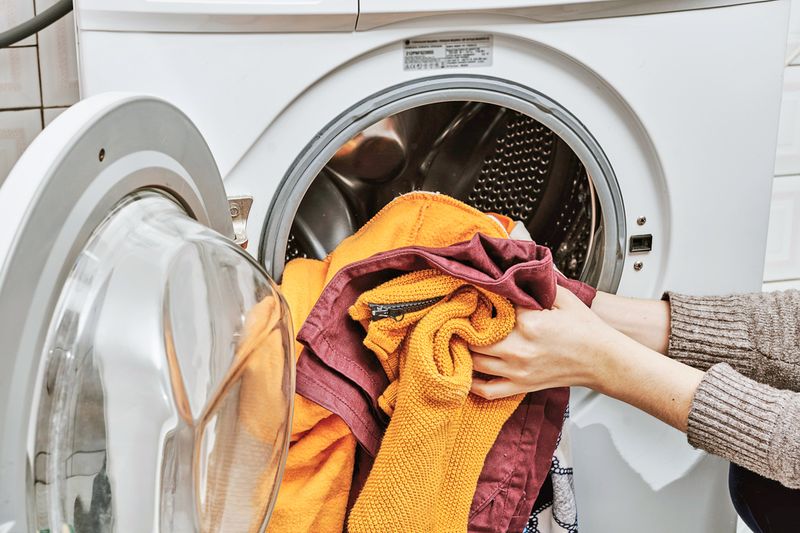 Anonymous person loading clothes into a washing machine.