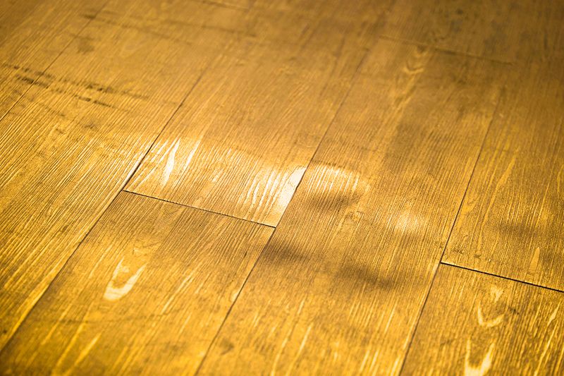 A close-up of a yellowish hardwood floor with several dents in it.