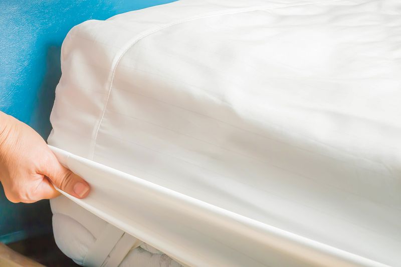 Close-up of an anonymous person putting a white fitted sheet onto a mattress.