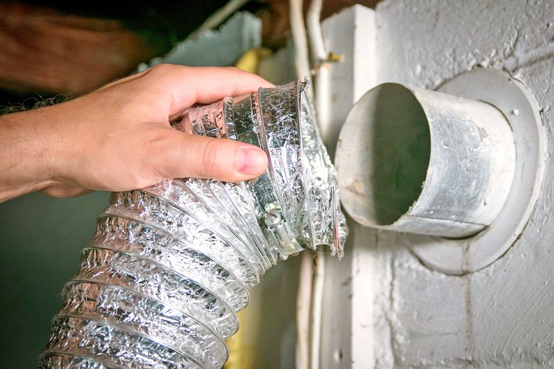 Anonymous person disconnecting a dryer vent hose from the back of the appliance.