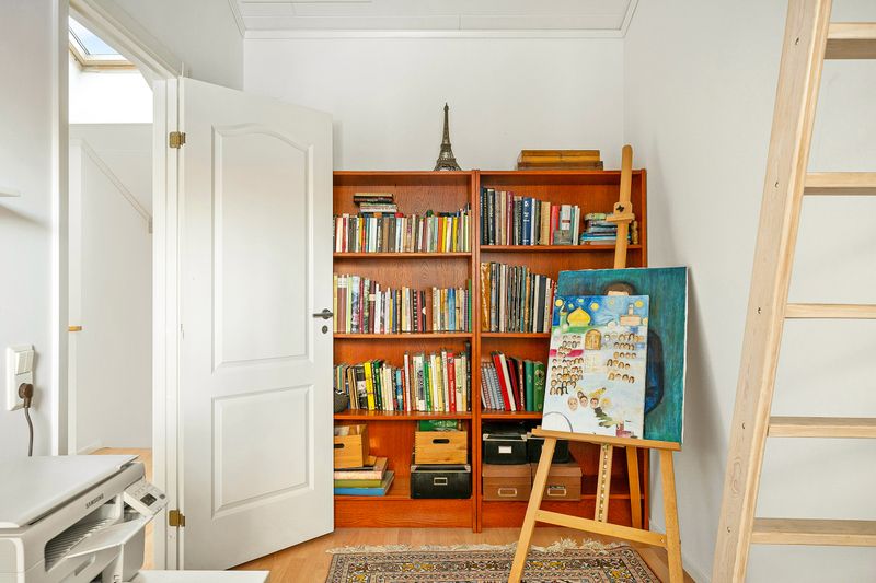 A white room with two wooden bookcases side-by-side. In front of them is an easel with a painting on it.