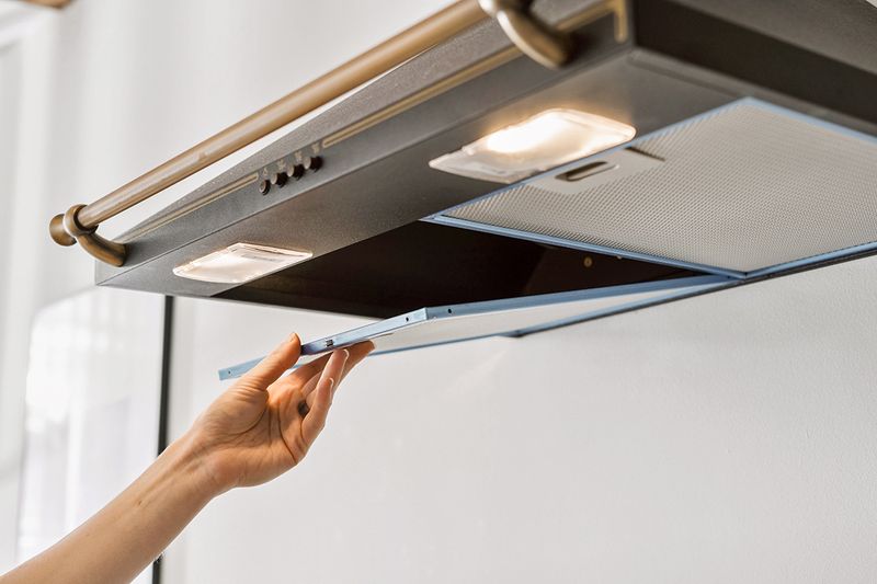 Anonymous person removing a range hood filter from a stainless steel range, presumably for cleaning.