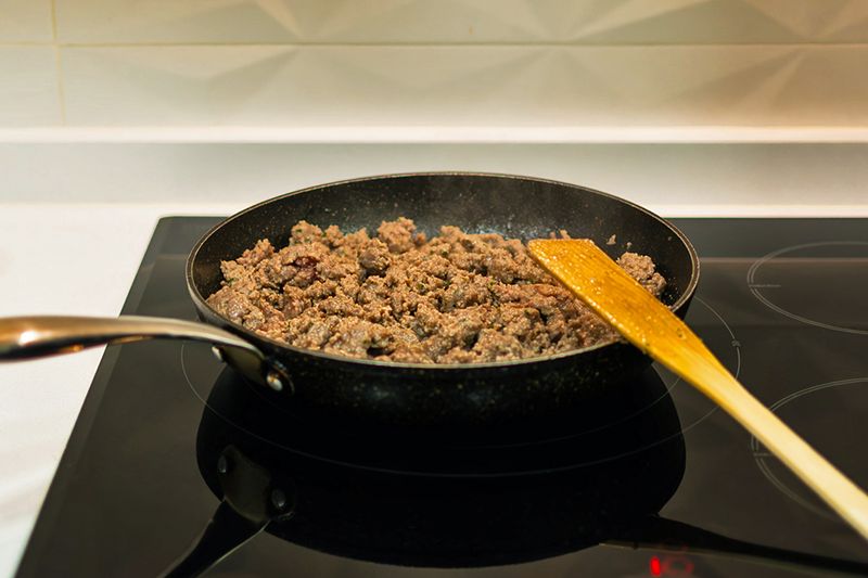 A skillet filled with browned ground beef on a glass cooktop.