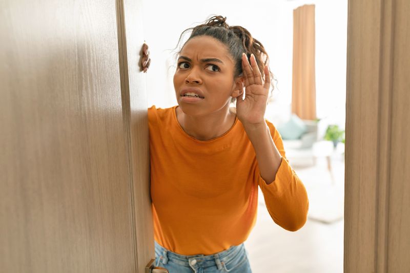 A young woman cupping her ear to hear something better. She looks concerned and is standing in an open doorway.