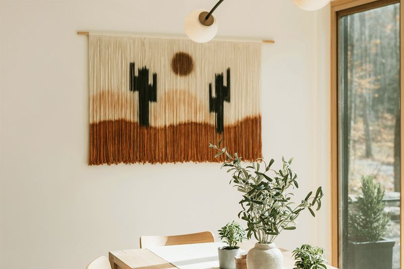 A desert-themed string tapestry on an otherwise blank wall in a dining room.