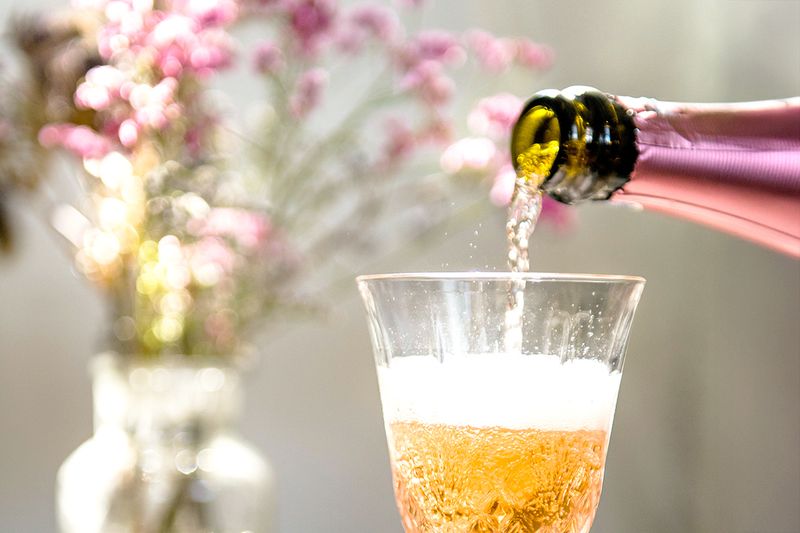 A close-up shot of bottle of Champagne being poured into a glass flute with flowers in the background.