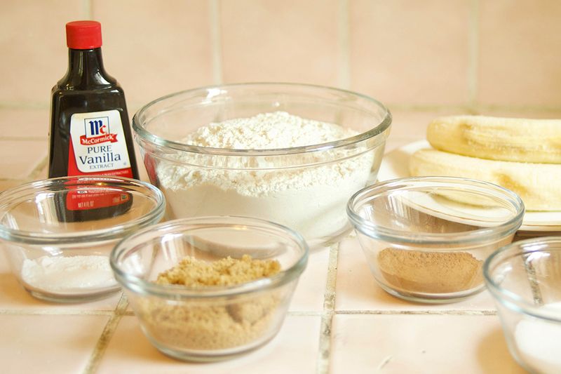 Baking ingredients, including flour, brown sugar, cinnamon, baking powder, and a bottle of vanilla extract, all laid out on a countertop.